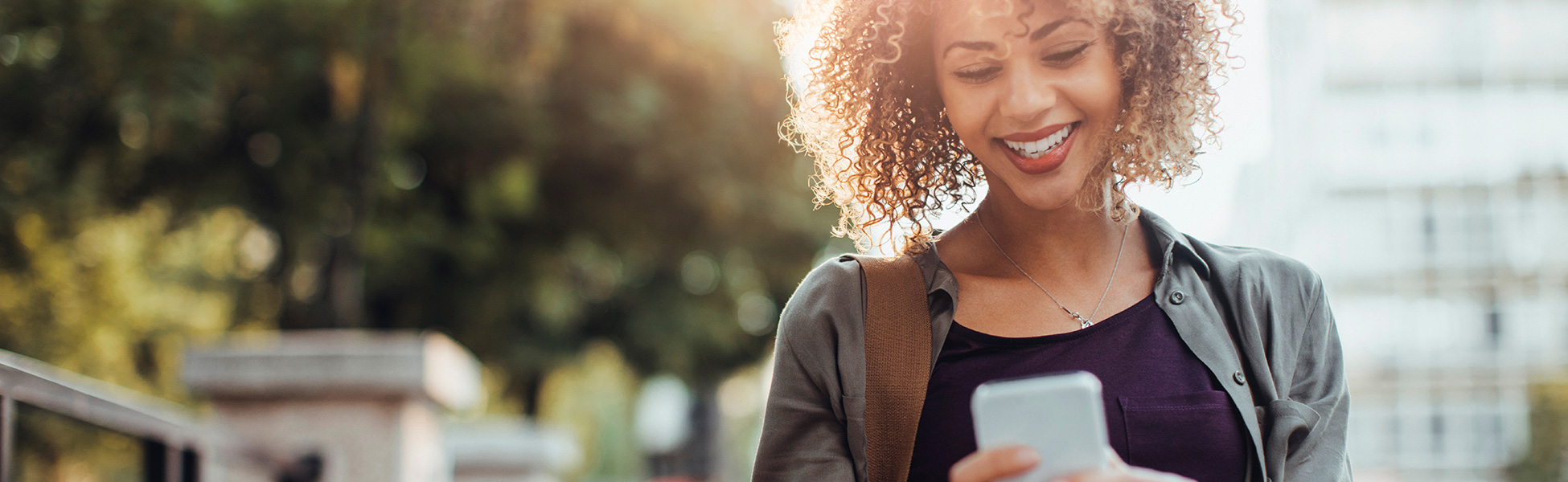 Woman smiling while looking at her phone outdoors